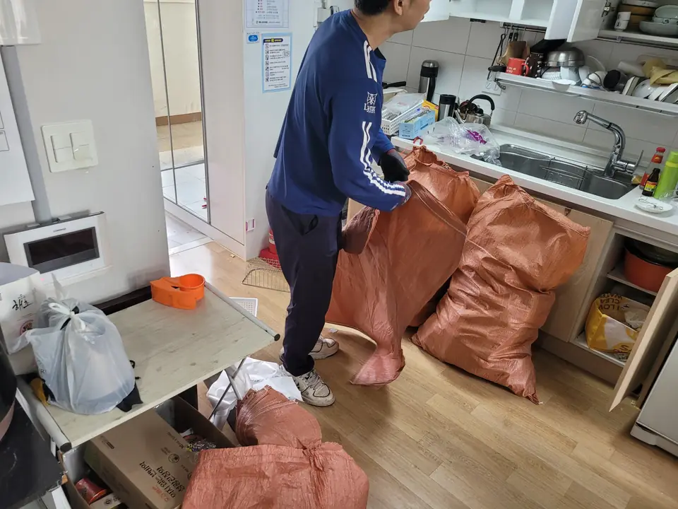 침대가 놓인 방에서 작업자가 물품을 마대에 담는 모습