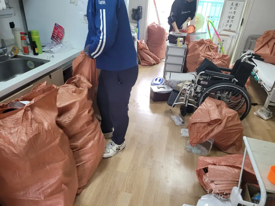 방에서 작업자가 마대 사이에서 물품을 분류하는 모습